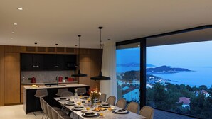 Una cocina moderna con comedor, amplios ventanales con vista al mar y una mesa dispuesta para el desayuno.
