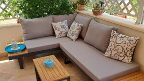 Ein modulares Sofa mit floralen Kissen, ein kleiner Holztisch mit einem blauen Gegenstand und ein Topf mit einer Pflanze auf einem Balkon.