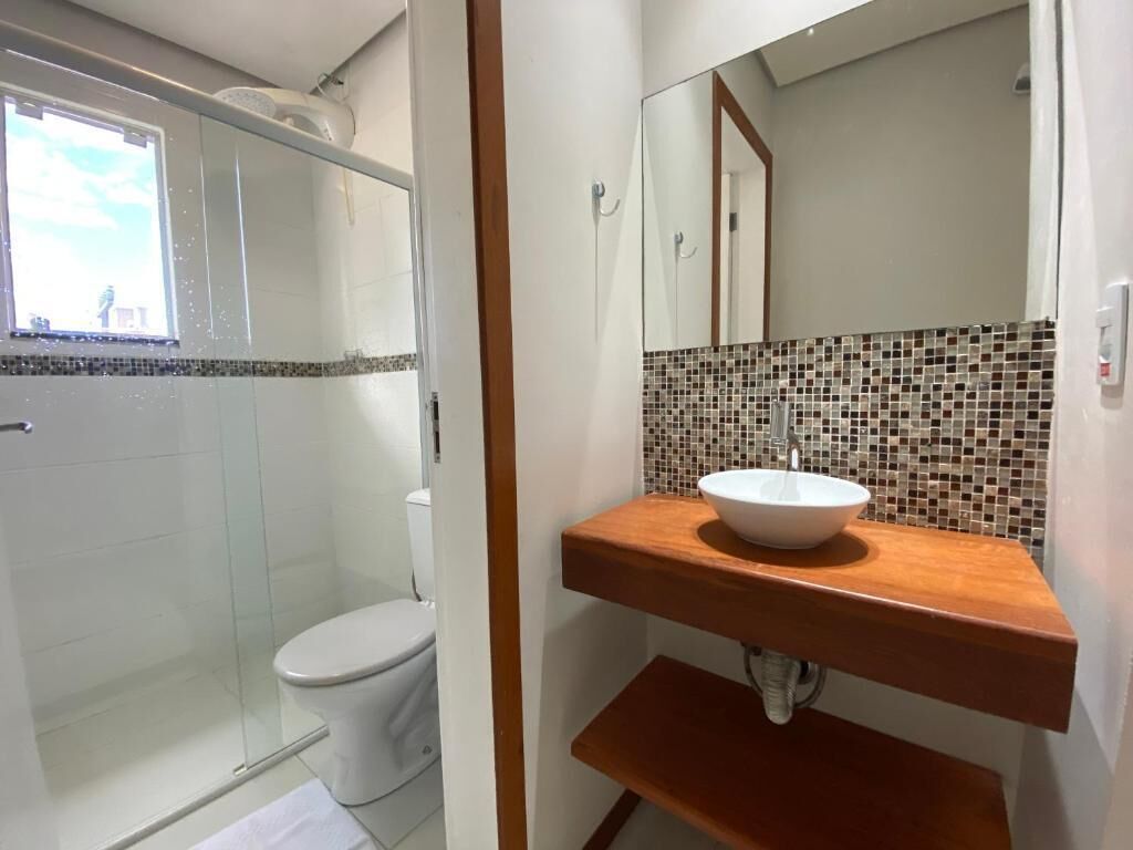 Ein Badezimmer mit Duschkabine aus Glas, einer weißen Toilette, einem Holzwaschtisch mit Mosaikfliesen-Spritzschutz und einem Spiegel über dem Waschbecken.