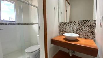 Ein Badezimmer mit Duschkabine aus Glas, einer weißen Toilette, einem Holzwaschtisch mit Mosaikfliesen-Spritzschutz und einem Spiegel über dem Waschbecken.