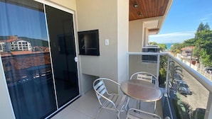 A balcony with a glass door, a small table, and two chairs. - Parada Beach Apartamentos (Florianopolis)