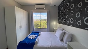 A modern hotel room with a large bed, a wardrobe, a window with a view, and a patterned wall. - Parada Beach Apartamentos (Florianopolis)