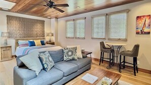 A modern living room with a sofa, a coffee table, a dining table with chairs, a ceiling fan, and a painting on the wall. - Sun 'n Sand Studio at Avila - a perfect beach spot! (Avila Beach)