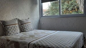 A bedroom with a bed, pillows, and a window with a view of greenery. - Charming T3 villa near the sea (Le Pradet)