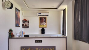 A reception desk labeled "Kala Retreat" with a clock, framed picture, air conditioning unit, and a framed photograph on the wall. - Kala Retreat (Rishikesh)