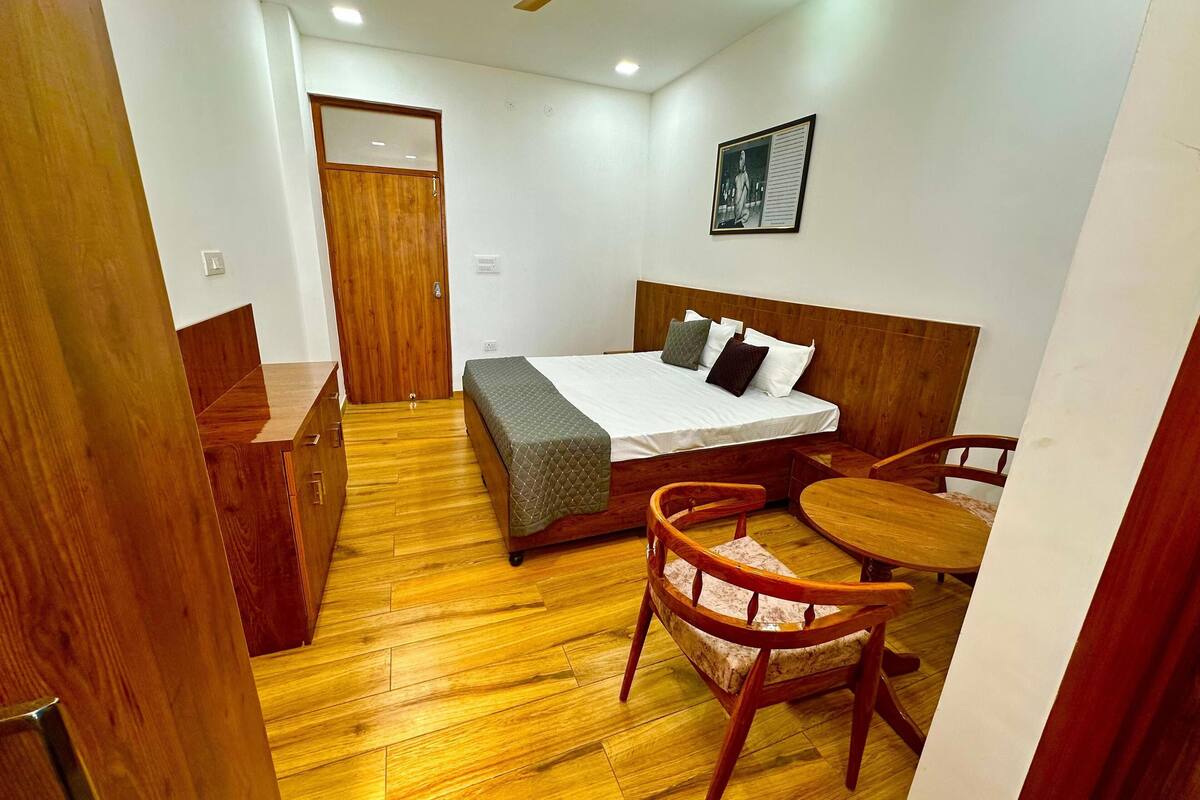 Une chambre d’hôtel compacte avec un plancher en bois, un lit recouvert d’une courtepointe matelassée, une tête de lit en bois, un bureau en bois, une chaise et un ventilateur de plafond.