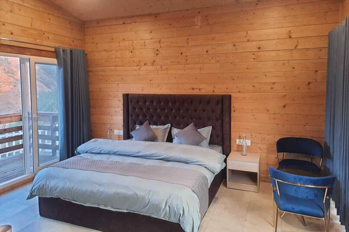 Een kamer met houten lambrisering, een bed, een stoel, een nachtkastje en een raam met gordijnen.