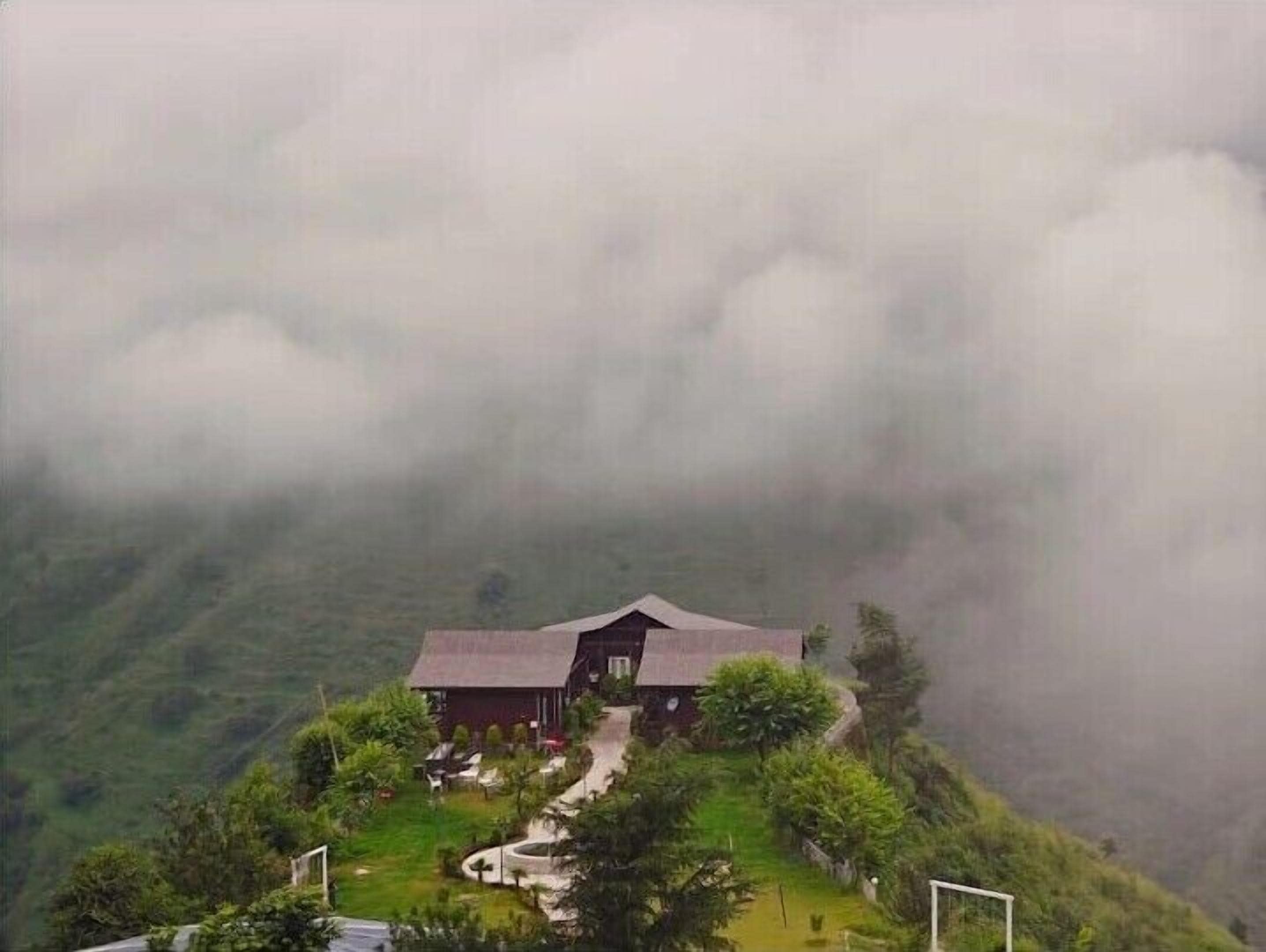 Une maison avec un toit en pente, entourée d’une végétation luxuriante et située au pied d’une pente abrupte.