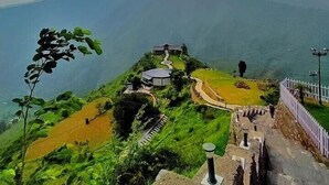 Un paysage montagneux avec un sentier menant à un bâtiment doté d’un toit circulaire, le tout entouré de verdure.