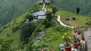 Une propriété située sur une colline, accessible par un sentier qui mène à un bâtiment, le tout entouré d’une végétation luxuriante et de champs en terrasses.