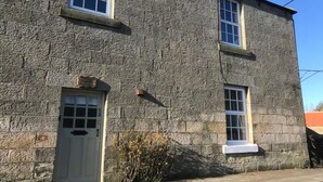 A stone building with two windows and a door, a sign above the door, and a small overhang above the windows.