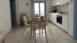 Cocina compacta con comedor, que incluye una mesa redonda con sillas de mimbre, vistas a través de una ventana y un horno empotrado.