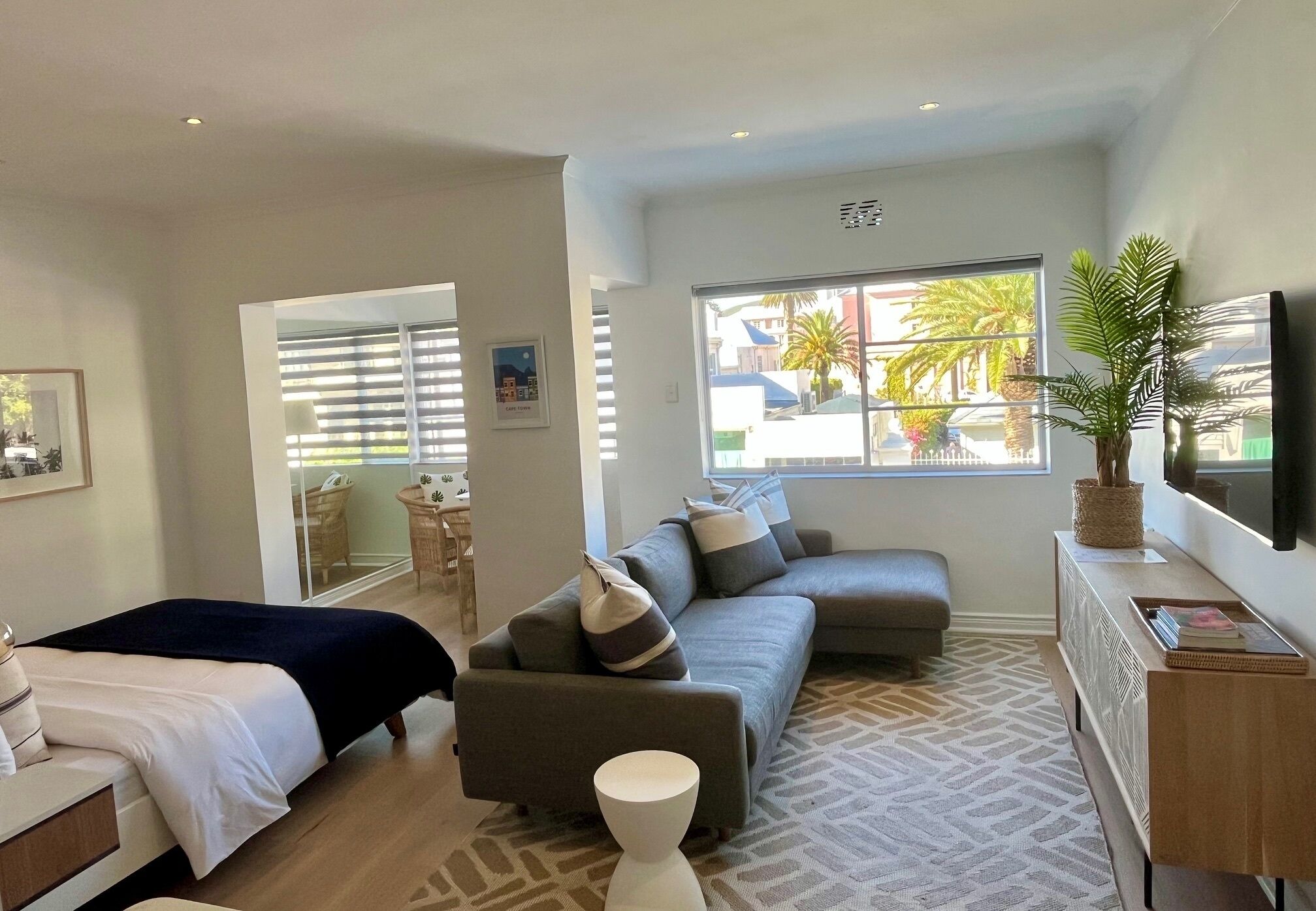 A modern hotel room with a bed, sofa, and a large window offering a view of palm trees.