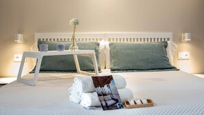 A neatly made bed with green and white bedding, a bedside table with a vase of flowers, and a tray of toiletries. - Apartments Plaza Mayor 35, 105 Family (Cáceres‎)