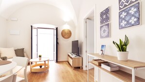 A bright living room with a wooden floor, a white sofa, a small round table, a TV on a wooden stand, and a potted plant. - Apartments Plaza Mayor 35, 105 Family (Cáceres‎)