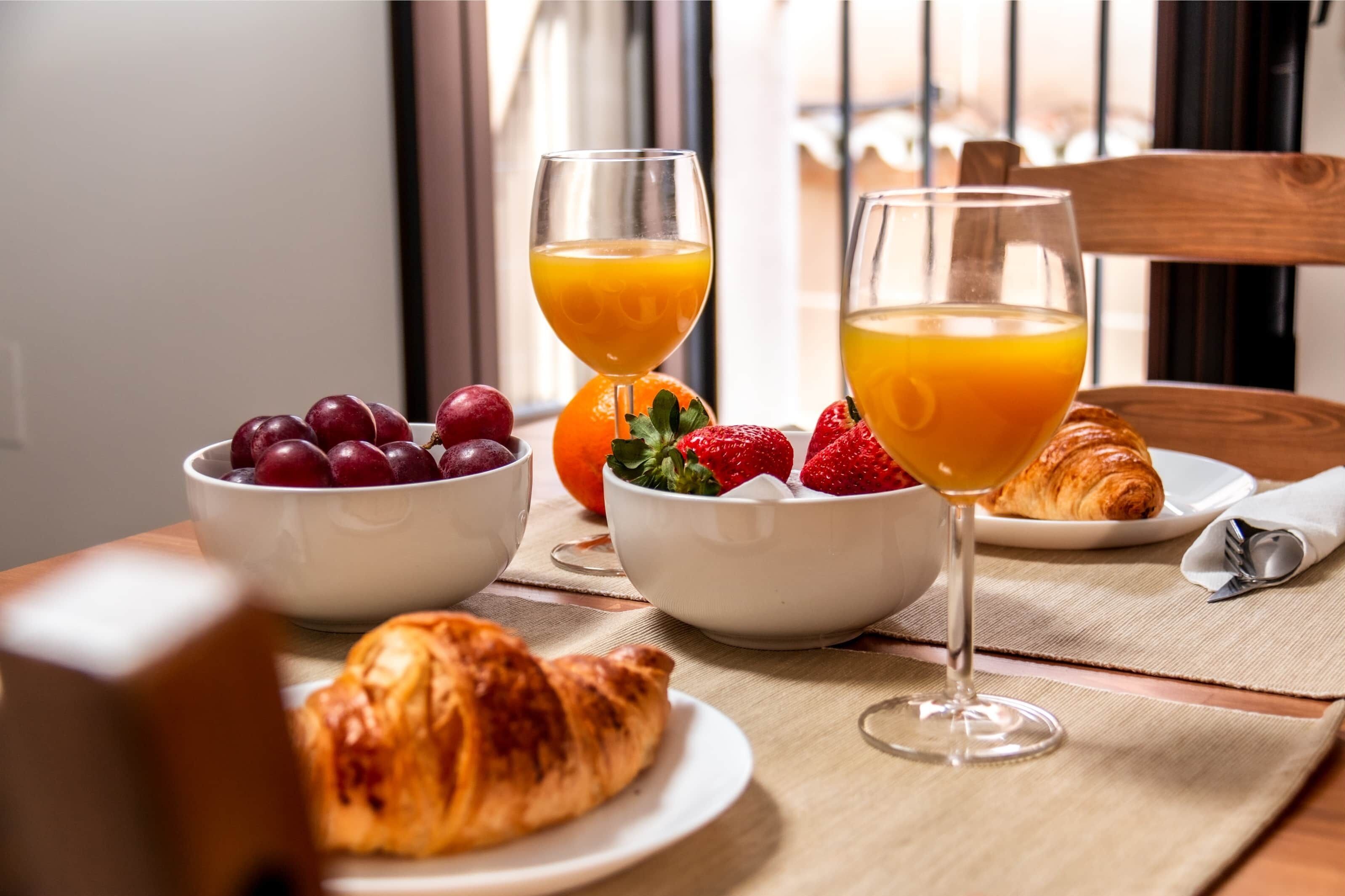 A breakfast setting with croissants, fruit, and orange juice on a table.