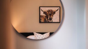 Una habitación con una lámpara redonda de pared, una obra de arte enmarcada de un toro y una silla verde.