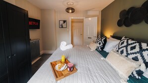 Una habitación de hotel con una cama, una bandeja con croissants y mermelada, un letrero de Netflix montado en la pared, y una puerta que da a otra habitación.