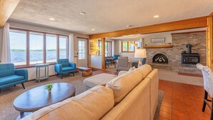 Una sala de estar acogedora con chimenea, asientos cómodos y ventanas amplias con vista a un cuerpo de agua.
