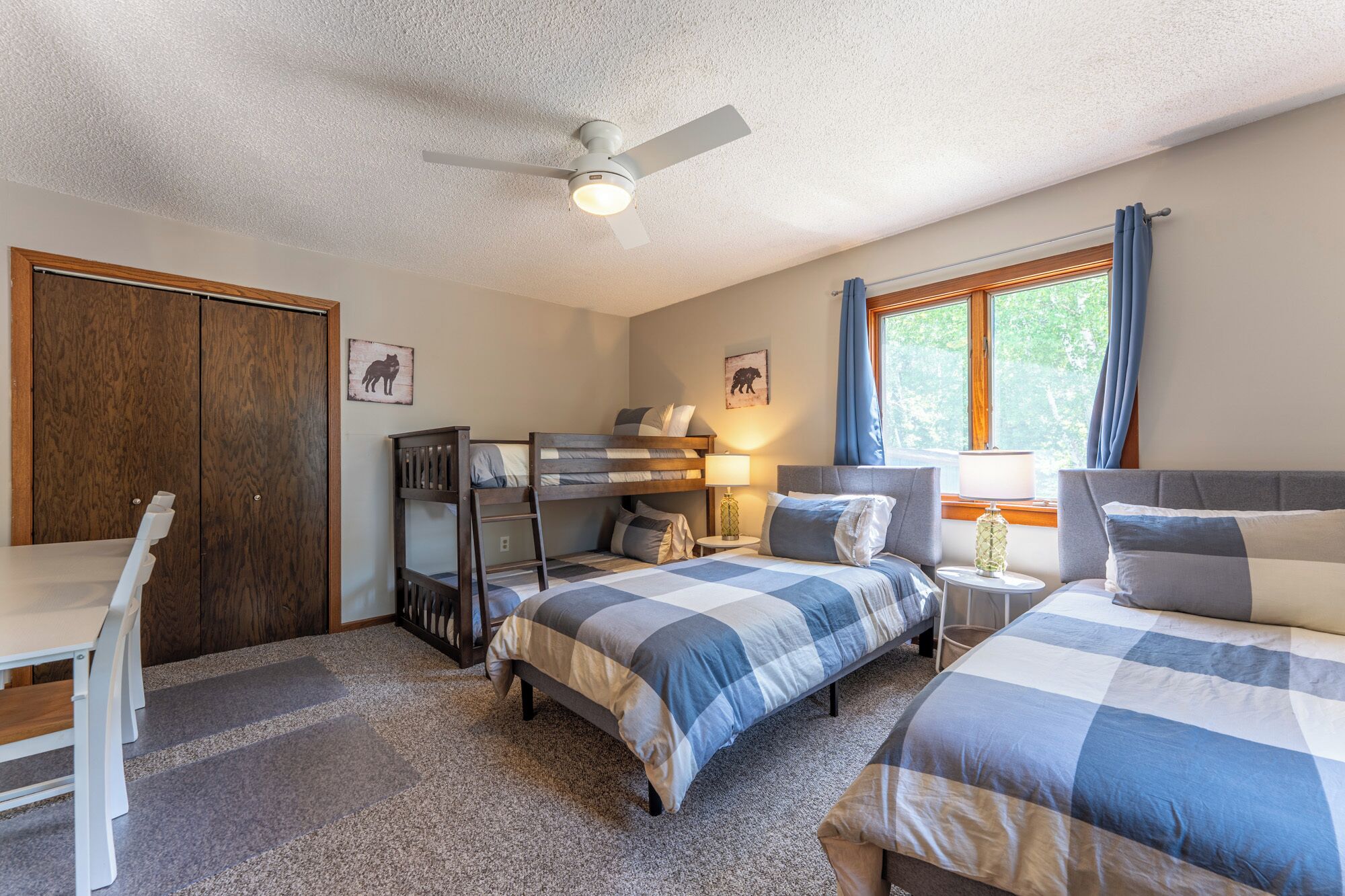 A bedroom with two beds, a desk, a wardrobe, and a ceiling fan.