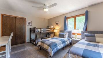 A bedroom with two beds, a desk, a wardrobe, and a ceiling fan.