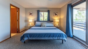 Un dormitorio con cama, dos lámparas de noche, ventilador de techo y un ventanal con cortinas.