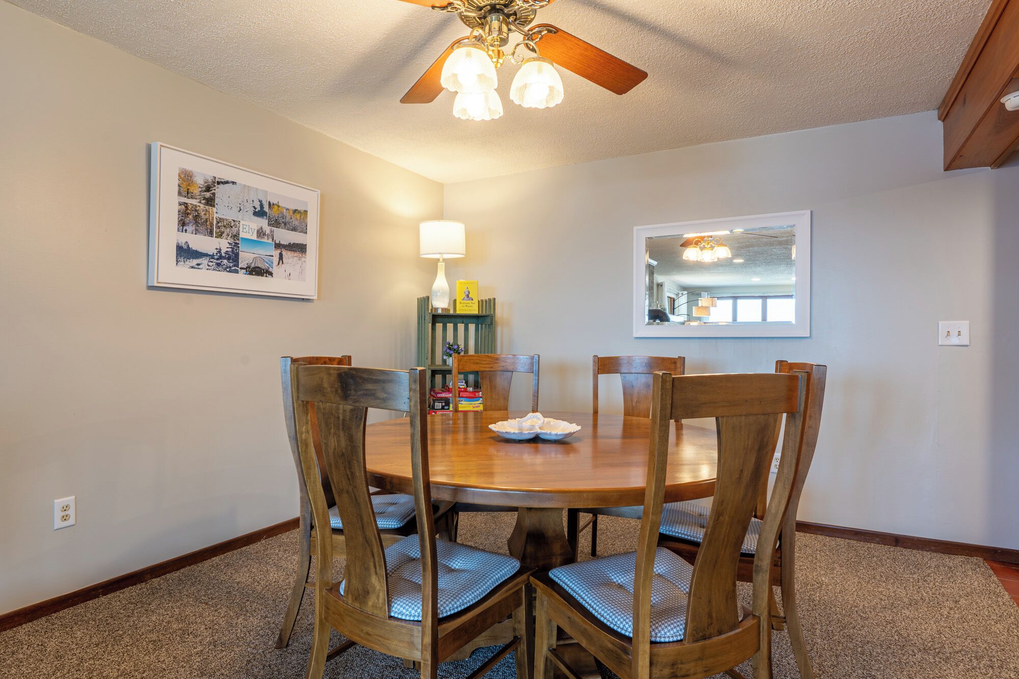 A dining area with a wooden table and chairs, a ceiling fan, and a framed picture on the wall.