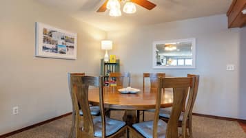 A dining area with a wooden table and chairs, a ceiling fan, and a framed picture on the wall.