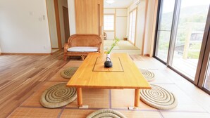 Une pièce de style japonais traditionnel, avec un sol recouvert de tatamis, une petite table en bois, un tapis tissé, une chaise en osier et une porte coulissante donnant sur une autre pièce.