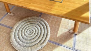 Une table en bois, sur laquelle on trouve un set de table en fibres tressées, une théière et un vase rempli de fleurs.