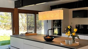 A modern kitchen with a large island, a built-in oven, and a black range hood. - Seaside holiday home (Grenaa)