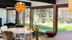 A modern kitchen with a large island, a dining area with a white table, and a view of the outdoors through large windows. - Seaside holiday home (Grenaa)