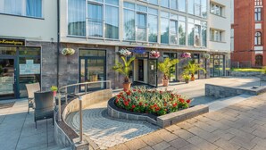 Un hôtel doté d’une façade moderne, d’un espace extérieur aménagé pour s’asseoir et de compositions florales.