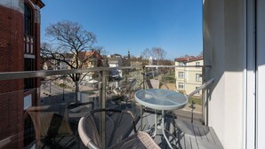 Un balcon avec une table ronde et des chaises en osier, donnant sur un quartier résidentiel avec des maisons et des arbres.