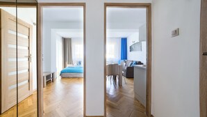 Une chambre d’hôtel moderne avec un plancher en bois, un lit recouvert d’une courtepointe bleue, un coin repas avec une table et des chaises, et un coin salon avec un canapé.