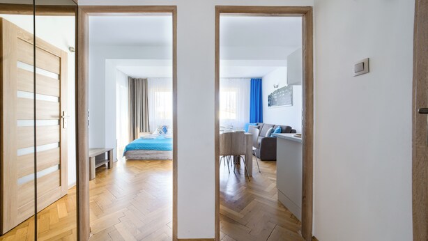 Une chambre d’hôtel moderne avec un plancher en bois, un lit recouvert d’une courtepointe bleue, un coin repas avec une table et des chaises, et un coin salon avec un canapé.