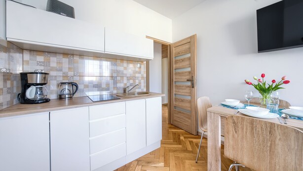 Une cuisine moderne avec des armoires blanches, un plan de travail en bois, une machine à café et un coin repas avec une table mise pour deux personnes.