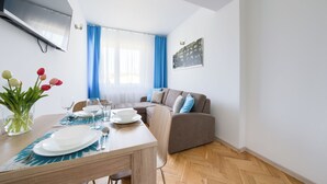 Un coin repas avec une table dressée pour deux personnes, un canapé et un téléviseur à écran plat fixé au mur.
