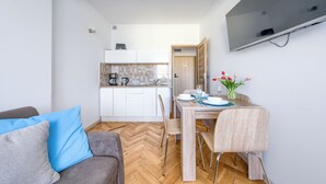 Un espace de vie compact comprenant un coin cuisine, un coin repas et un espace détente avec un canapé et des fauteuils.