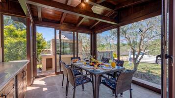 A dining area with a table set for breakfast, surrounded by wicker chairs, and large windows offering a view of the outdoors.