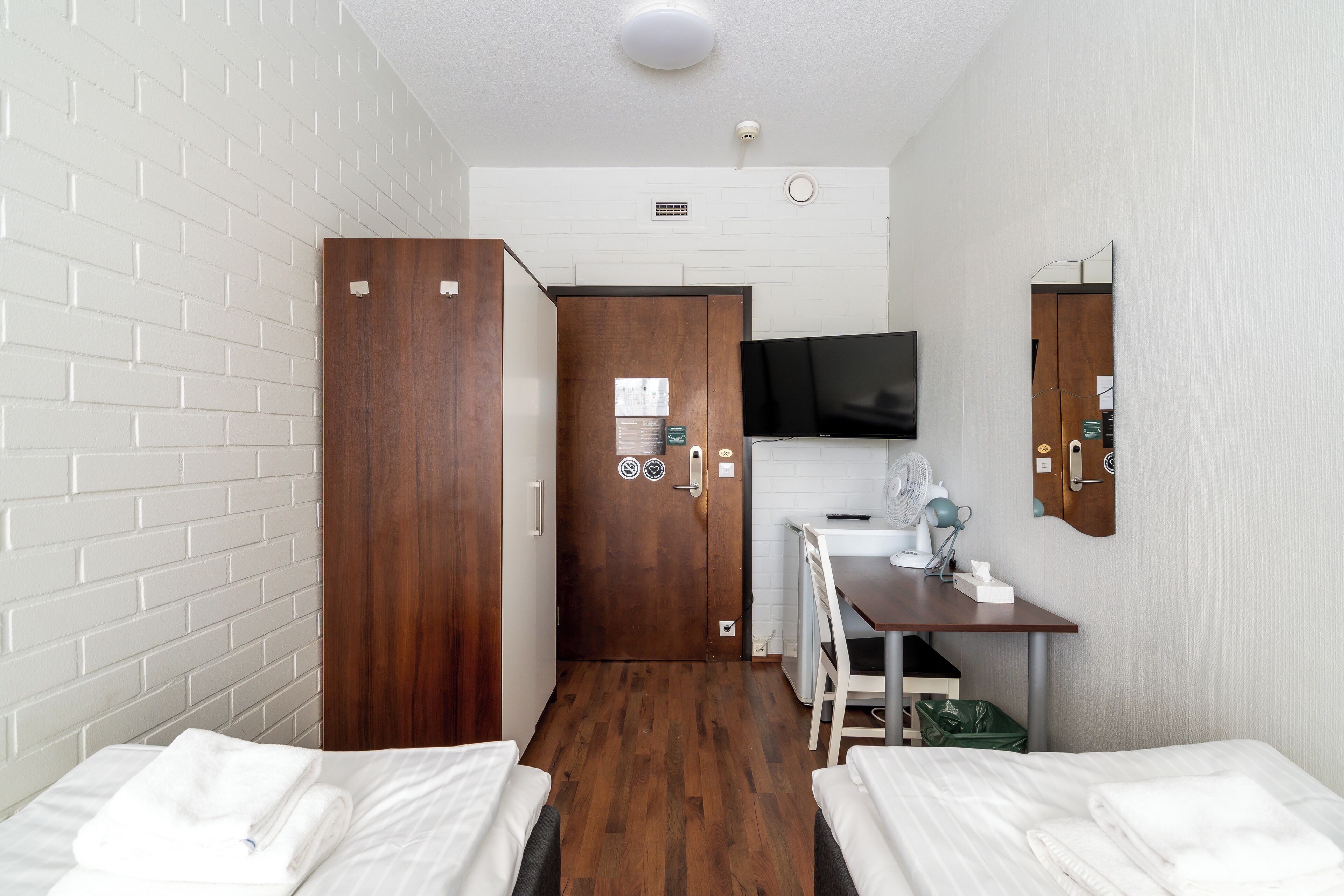 A hotel room with two beds, a desk with a chair, a television, and a mirror.