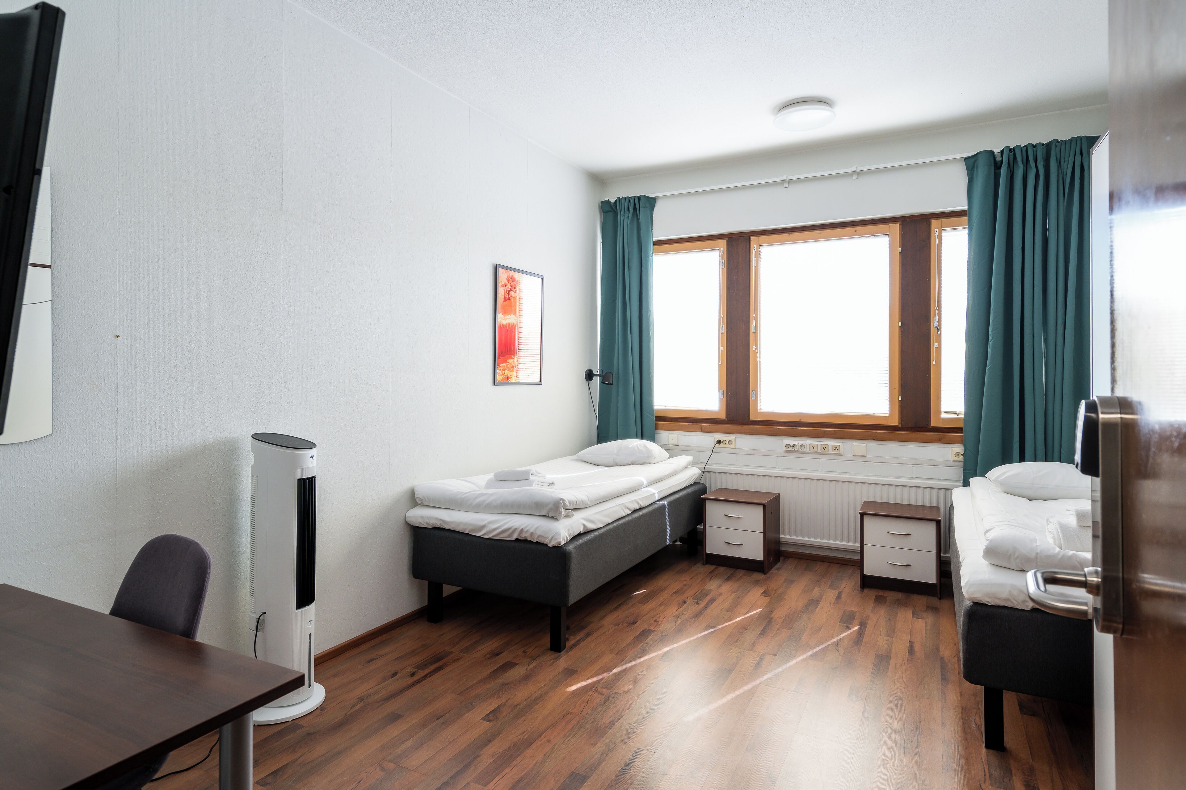 Quarto com cama, escrivaninha, cadeira, aquecedor e janela com cortinas.