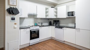 A modern kitchen with white cabinets, a stove, oven, microwave, and dishwasher. There are hanging pots and a framed certificate on the wall. - Hiisi Hostel Vihti - Private Rooms (Vihti)