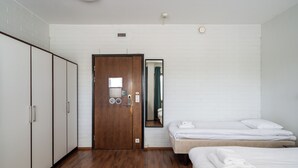 A hotel room with a wooden floor, a wardrobe, a bed with white bedding, and a mirror on the wall. - Hiisi Hostel Vihti - Private Rooms (Vihti)