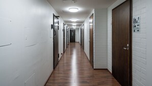 A long, narrow hallway with white brick walls and wooden flooring. There are doors on both sides, some with signs above them. - Hiisi Hostel Vihti - Private Rooms (Vihti)