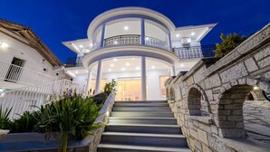 Una casa de varios niveles con un balcón circular central, paredes de piedra y una escalera que lleva a la entrada.