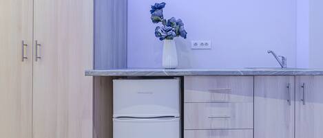 A compact kitchen with a PHILCO refrigerator, wooden cabinets, a white countertop, and a vase with flowers.