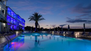 Una piscina iluminada en azul, con sillas de descanso y una palmera.