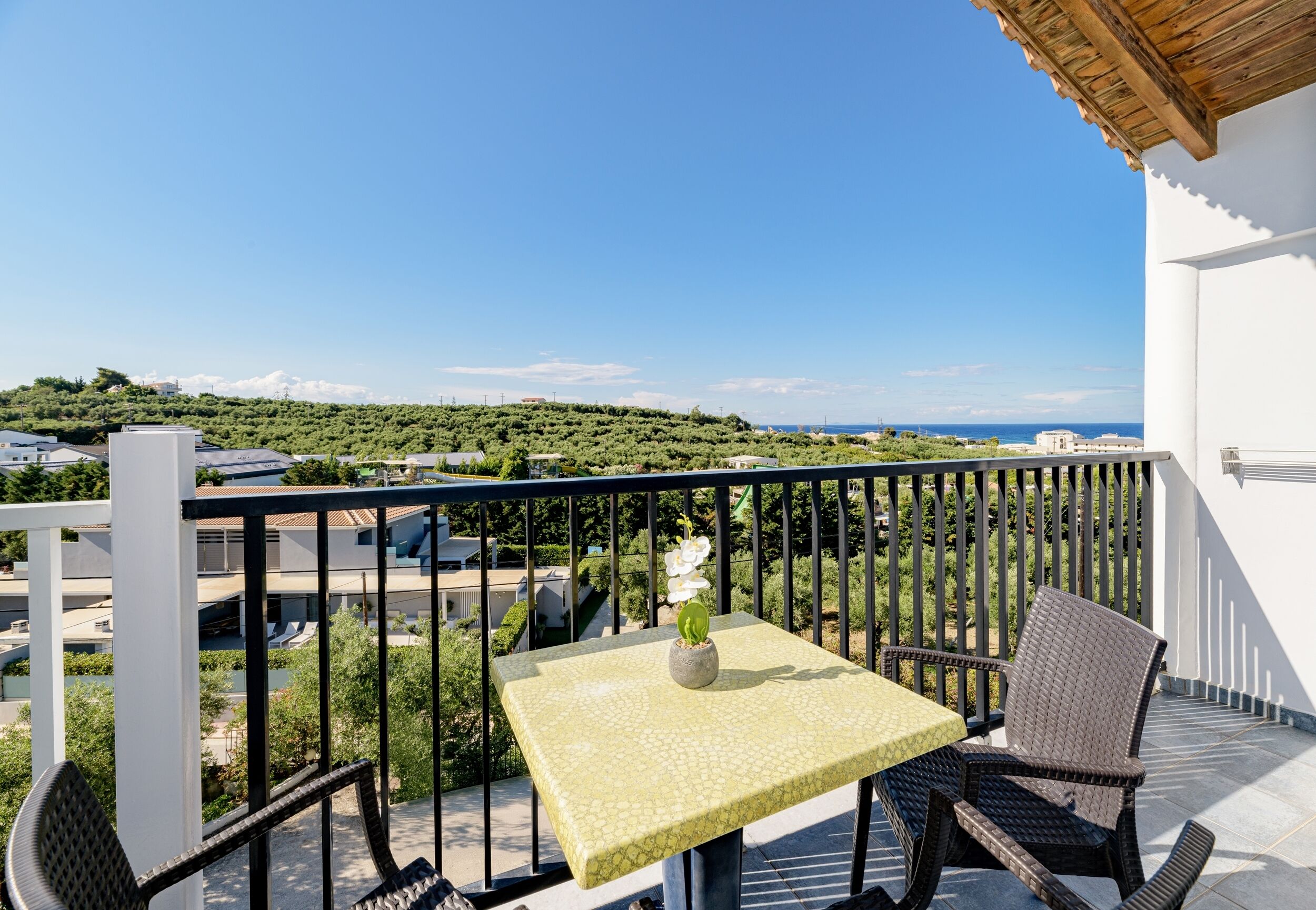 Un balcón con mesa y sillas, con vistas panorámicas a la costa y la vegetación.