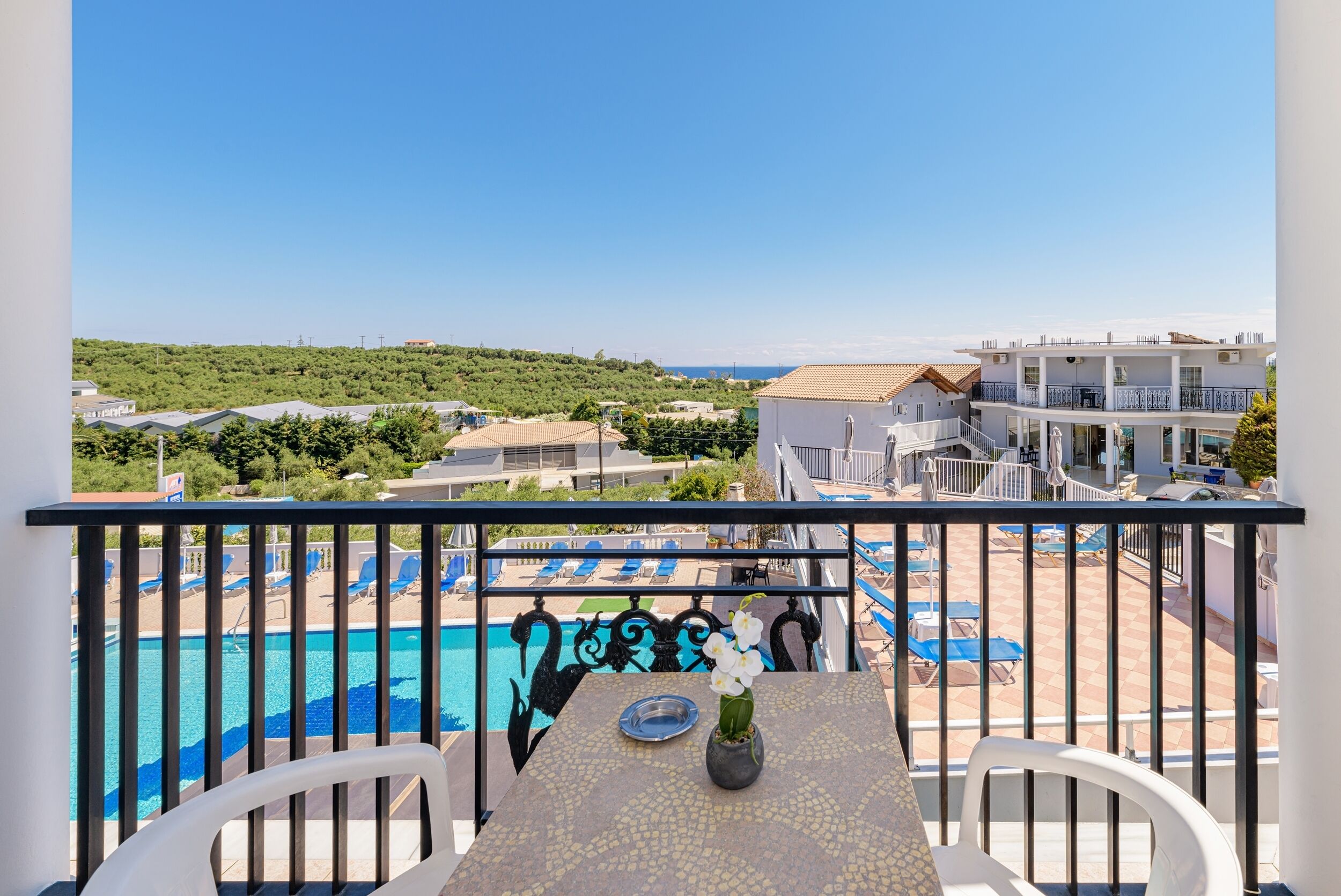 A balcony with a view of a swimming pool, lounge chairs, and a table with a vase of flowers.
